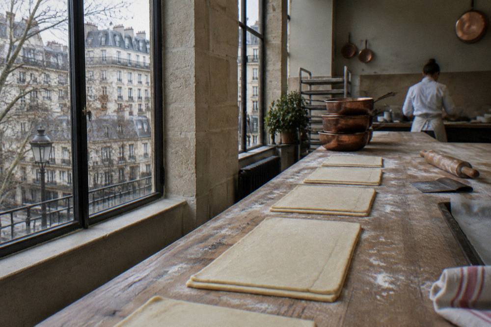 A baker's hands shaping croissant dough on a floured wooden bench