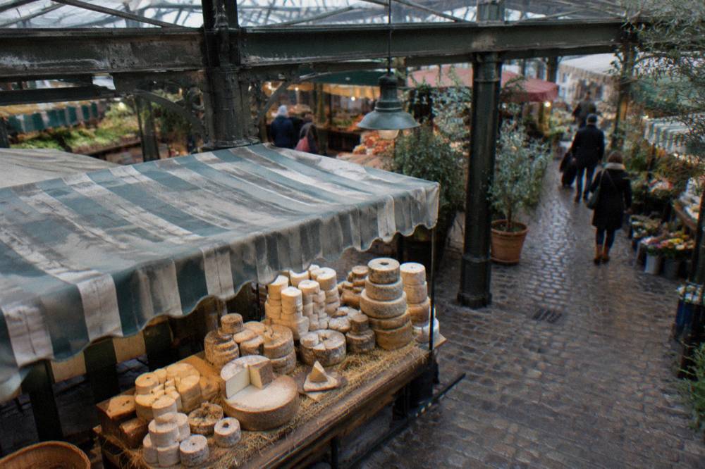 A market table stacked with cheeses under a striped awning in Paris