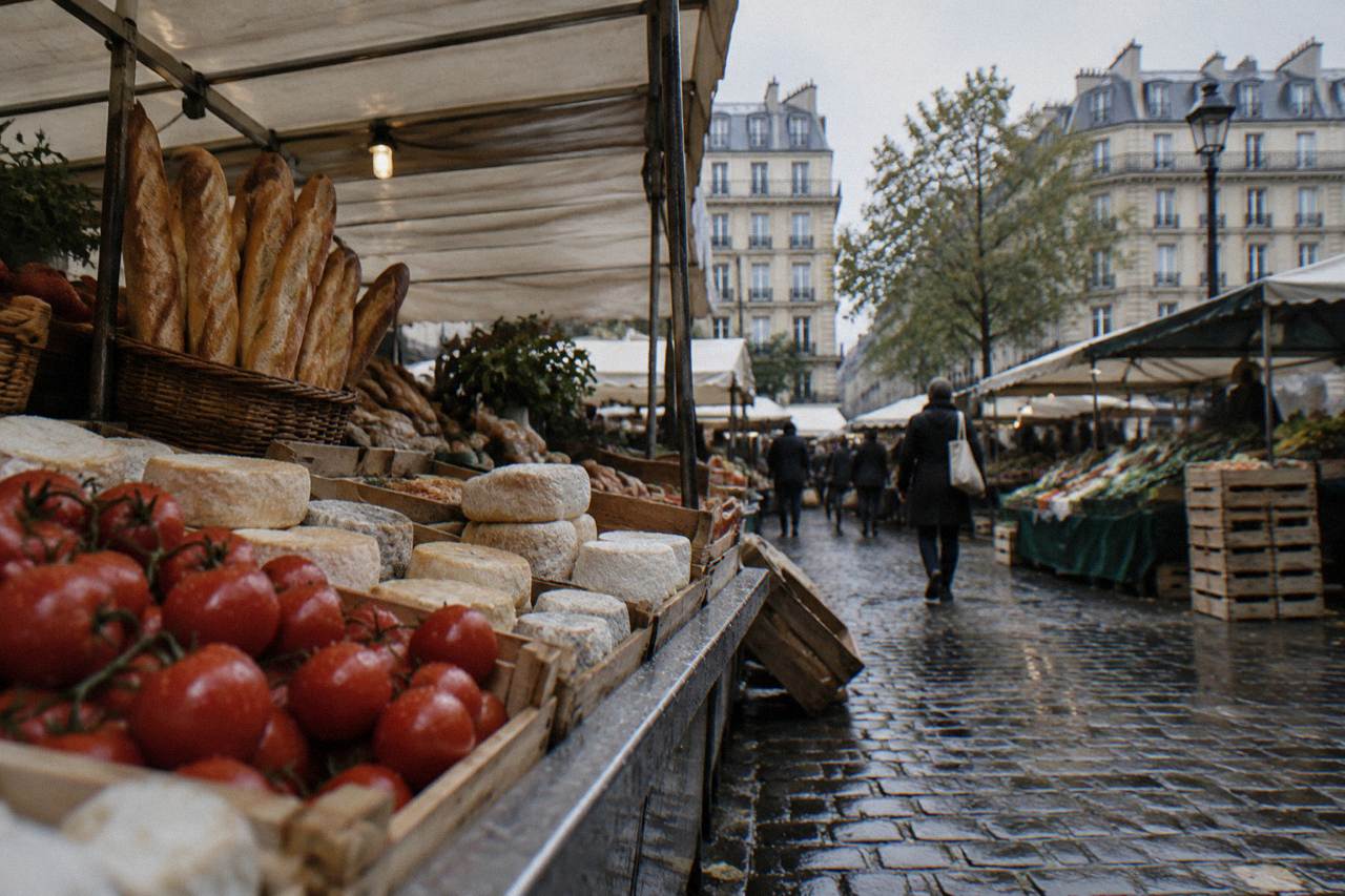 A Paris market stall with bread, cheese and produce arranged under awnings