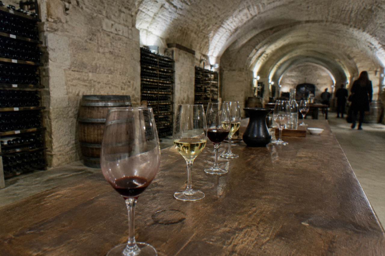 Glasses of red and white wine lined up on a wooden tasting table in a Paris cellar