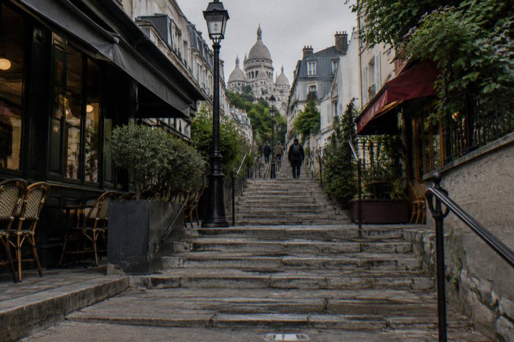 Stone steps climbing a narrow Montmartre street between cafe fronts