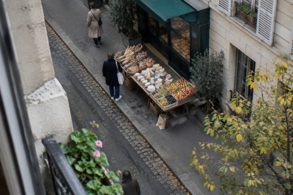 A wooden market table with bread, cheese wedges and fresh fruit