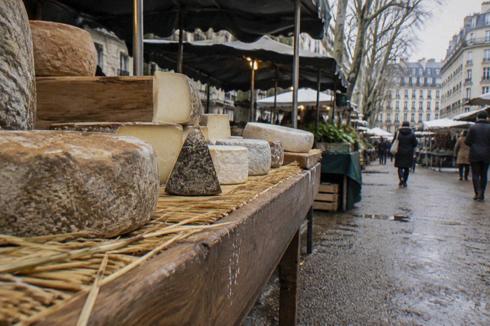 A wooden cheese counter in a Paris fromagerie with wheels and wedges of cheese arranged on straw