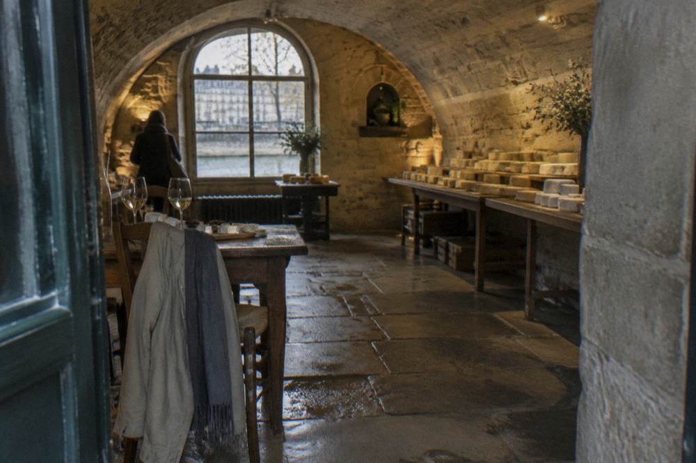 Light jacket and scarf draped over a chair beside a table of wine glasses and a cheese board