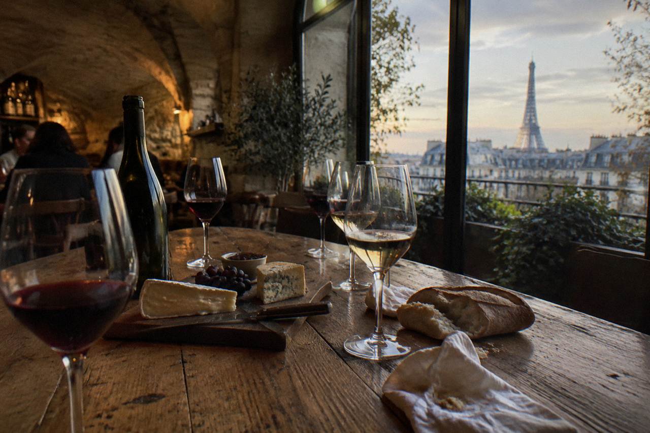 Wooden table set with wine glasses, a cheese board and a baguette in a softly lit tasting room