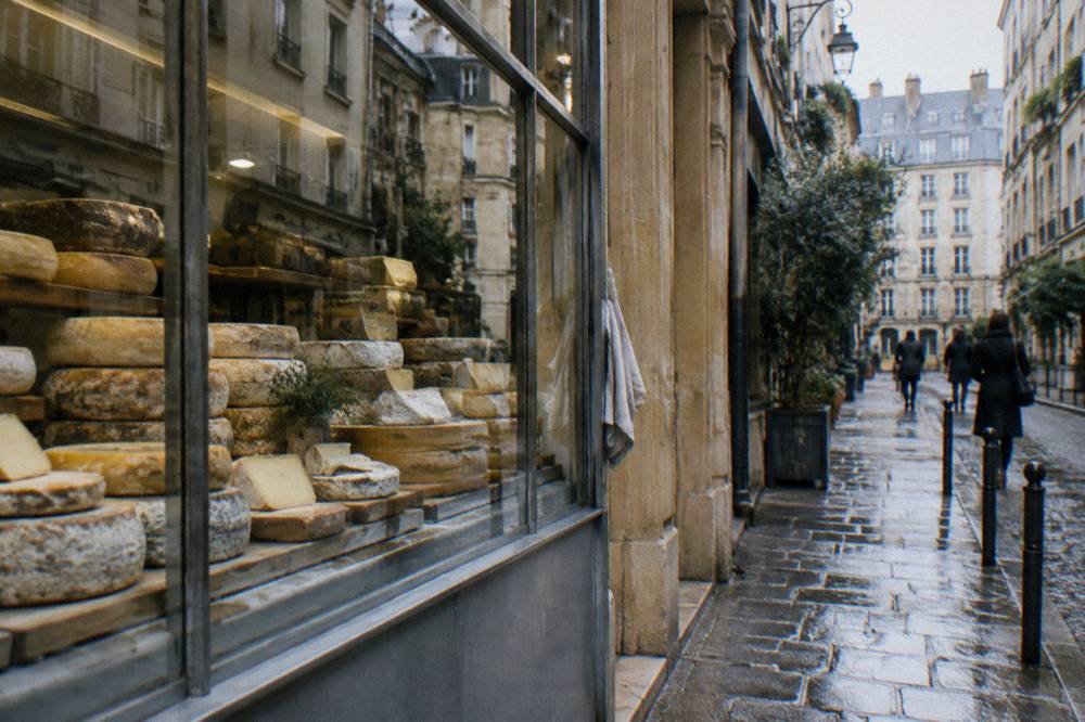 Cheesemonger counter with rows of labeled French cheeses behind glass