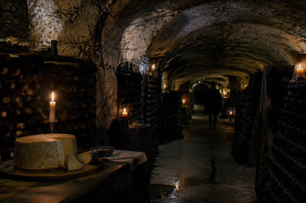Candlelit cheese cellar with wine bottles racked along stone walls