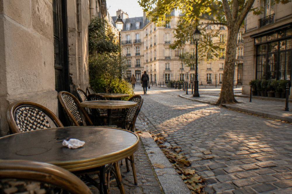Cafe tables and chairs set out on a cobblestone street beside old stone buildings