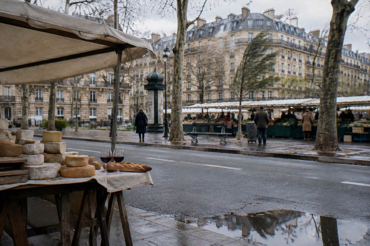 A Paris market table with cheeses, a baguette and glasses of red wine