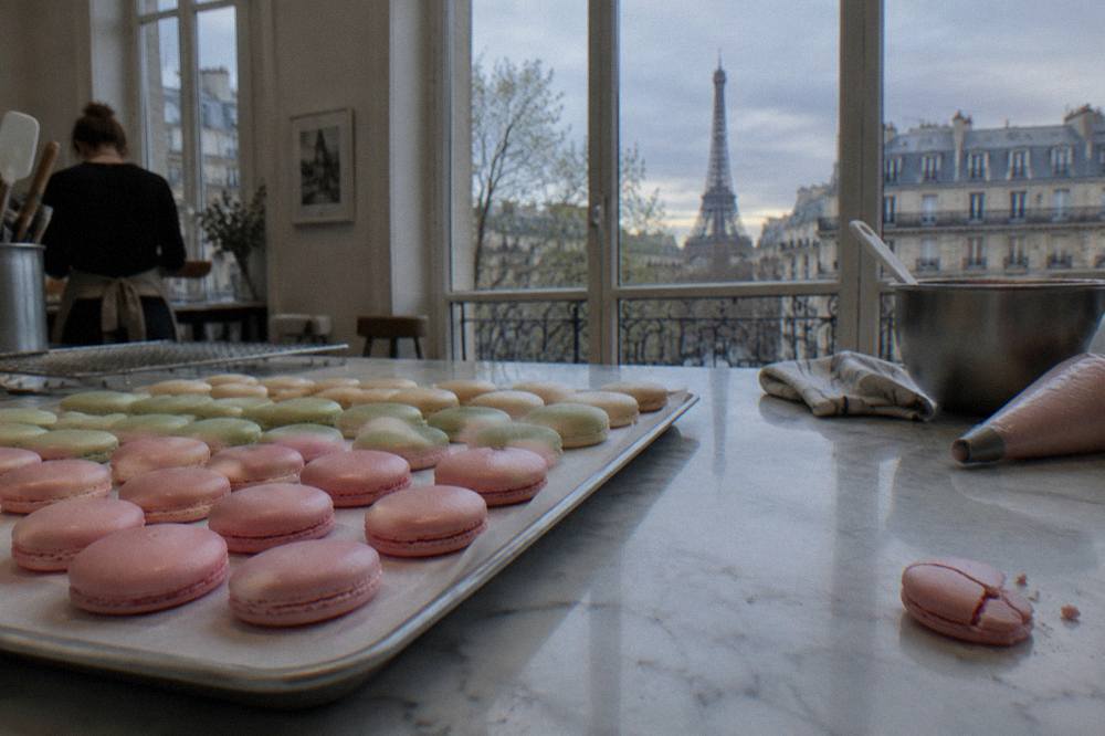 Close-up of pastel macaron shells arranged in neat rows on a marble counter