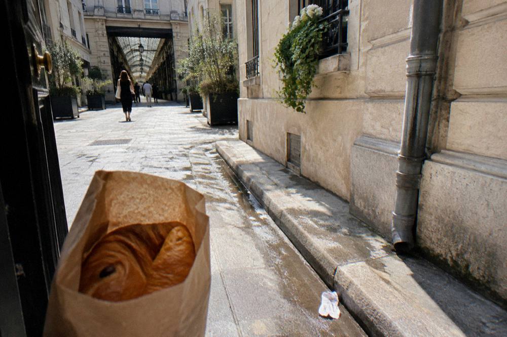 Paper bag of fresh pastries carried along a Paris street in late morning light