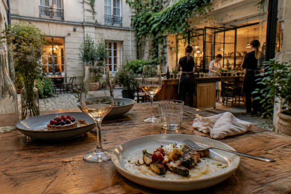 A rustic kitchen table set with a three-course French dinner and glasses of wine