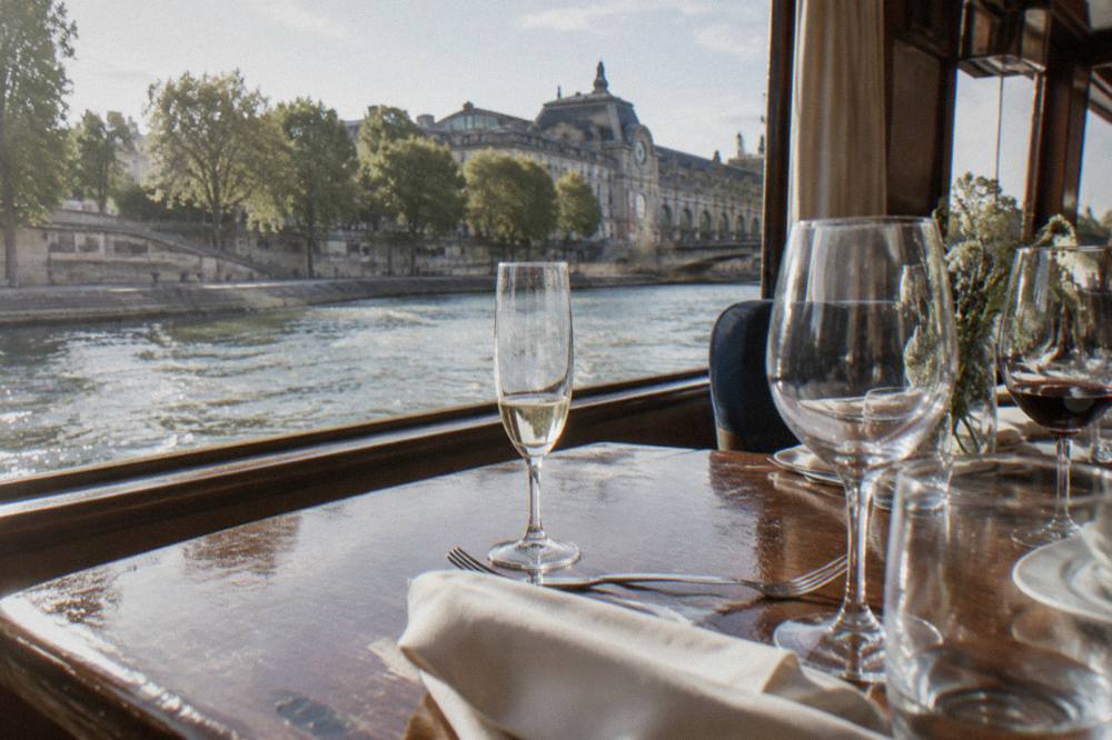 A set dinner table on a cruise boat with wine glasses and folded napkins beside a window
