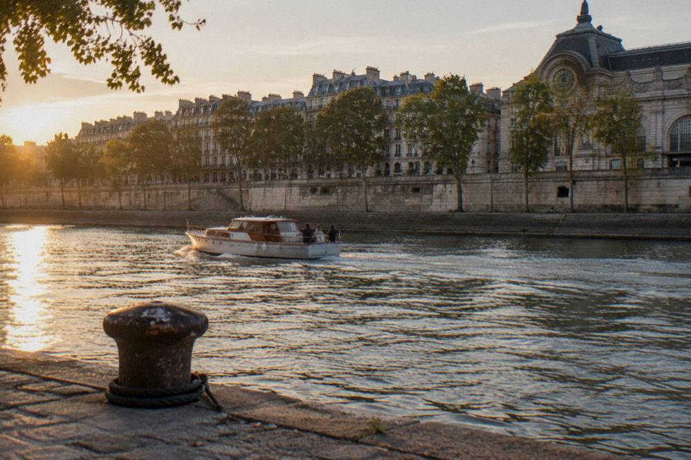 A small private boat on the Seine passing stone embankments in late afternoon light