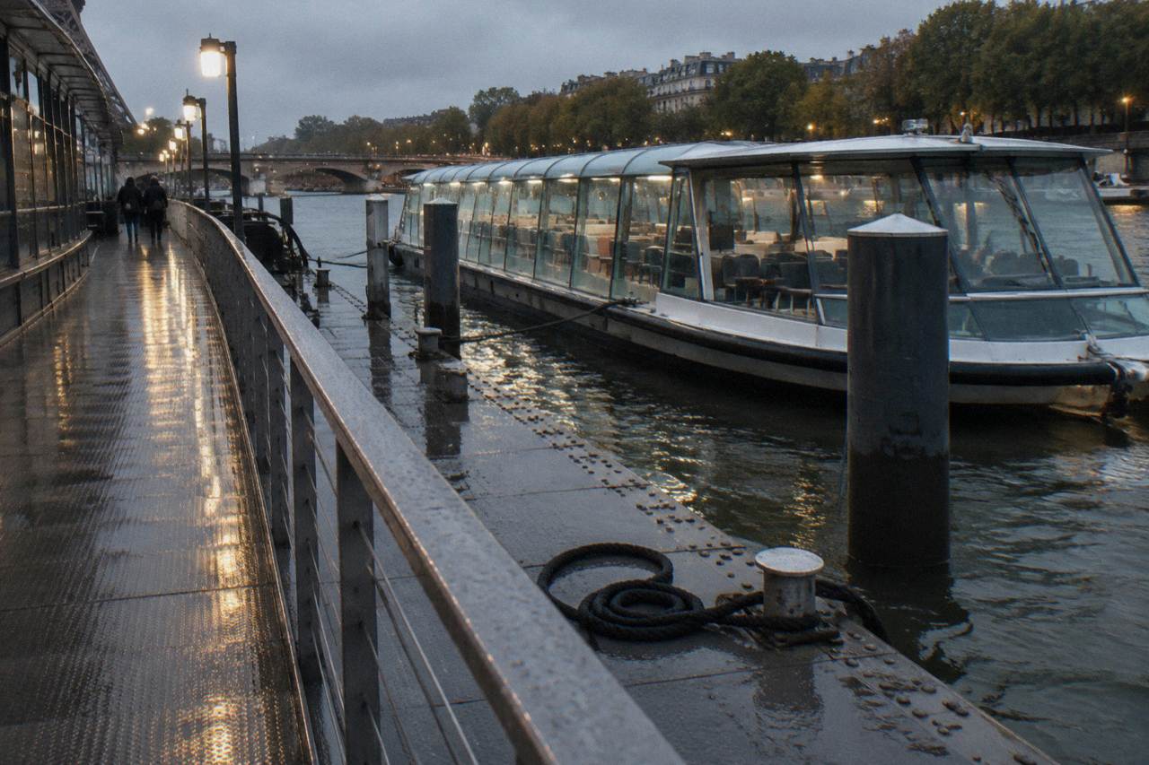 A glass-enclosed cruise boat on the Seine at dusk with city lights reflected on the water