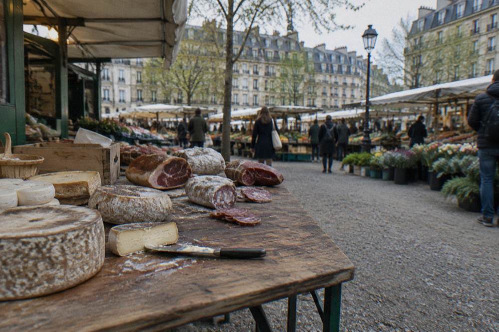 Cheese wheels and charcuterie slices arranged on a wooden market tasting board
