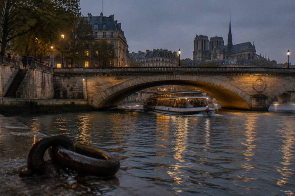Dinner cruise boat passing under a Seine bridge at dusk with city lights