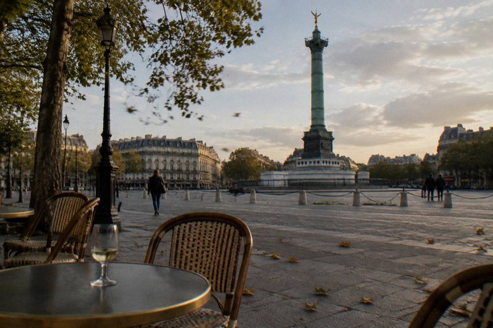 Café tables and chairs on a cobbled Marais square in late afternoon light