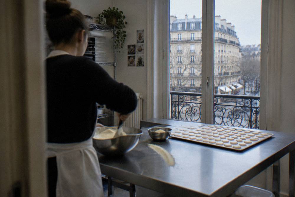 A chef instructor demonstrating macaron batter folding to a kitchen workbench