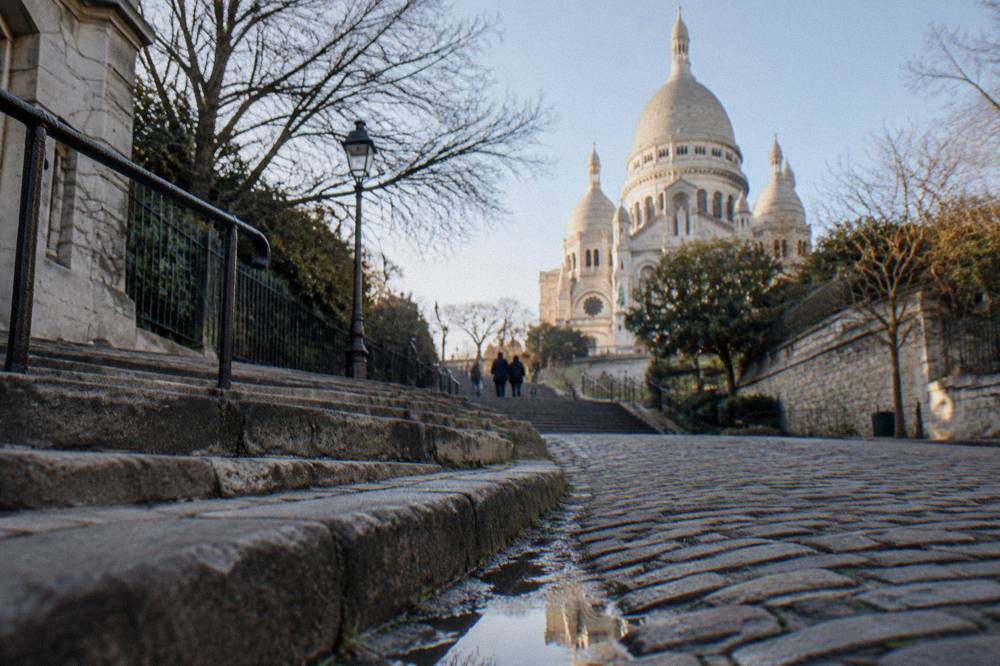 Cobbled Paris street rising toward a white domed basilica at the top of the hill
