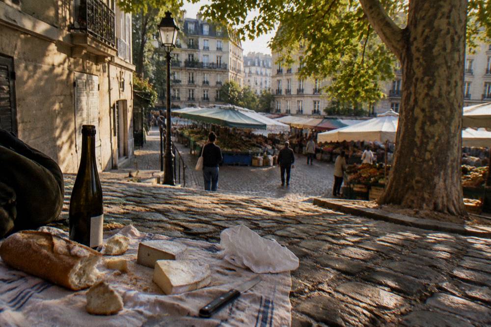 A picnic spread of bread, cheese and wine on a bench near a Paris market
