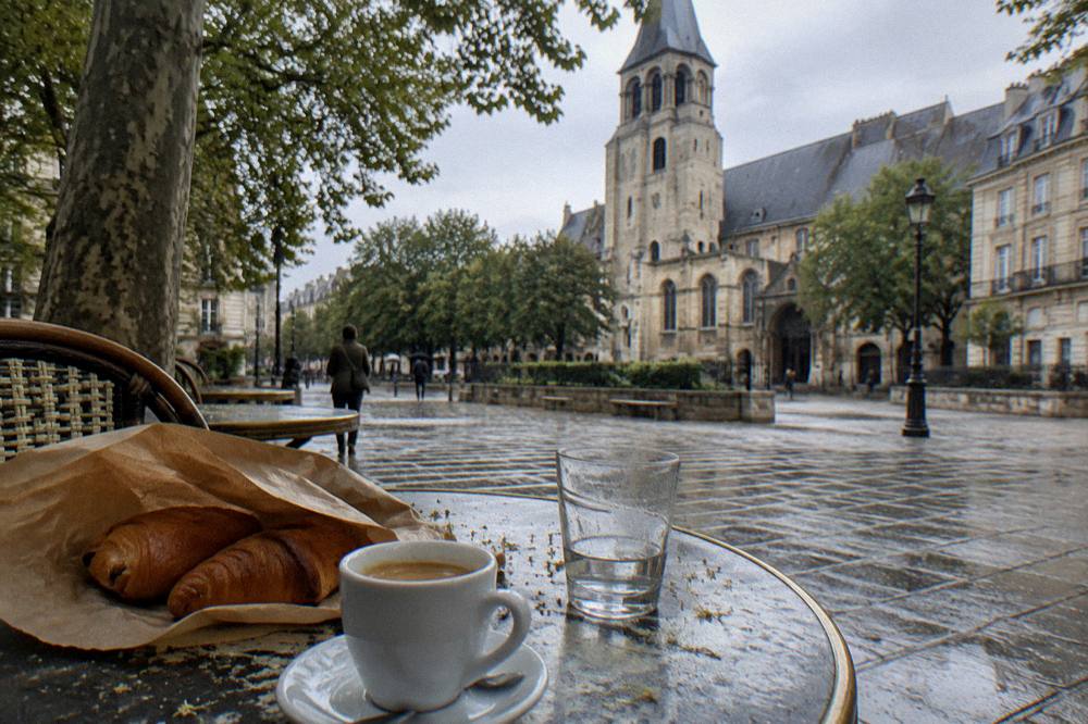 Paper bag of fresh pastries on a cafe table beside an espresso cup