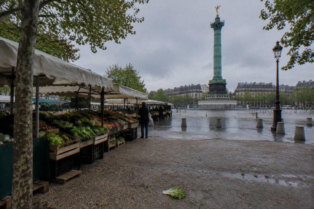 Market stalls with fresh produce under awnings beside a Paris square