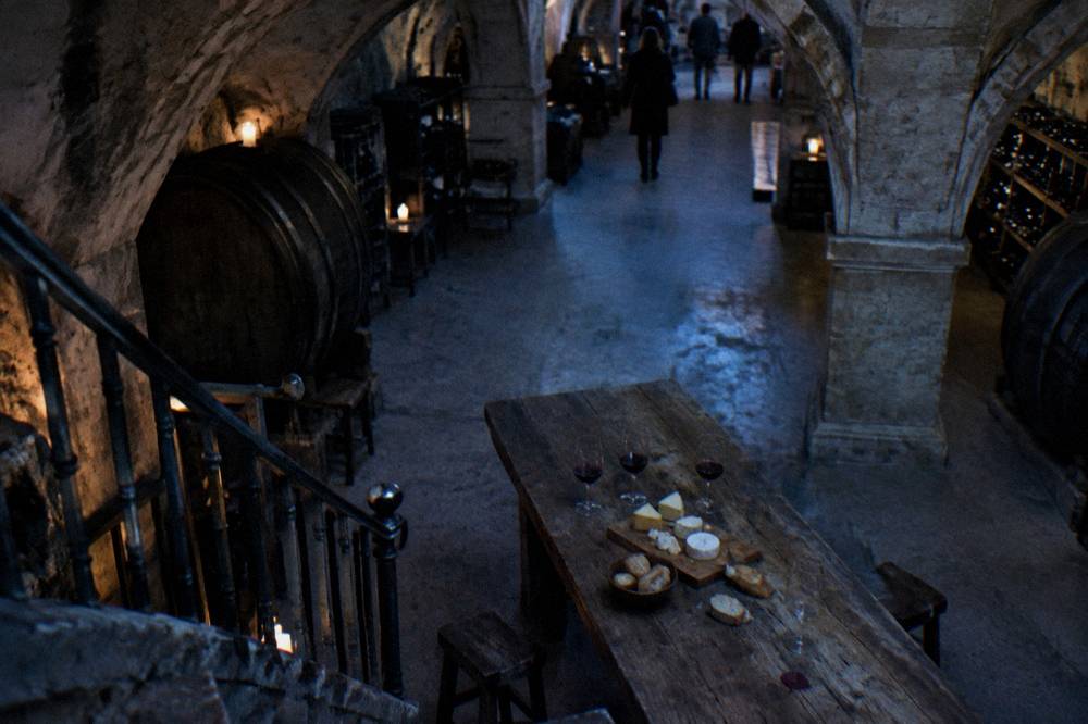 Cheese cellar tasting table with labeled cheese wedges, three wine glasses, and slices of baguette